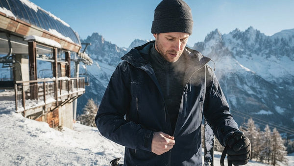 Skier at the top of a chairlift zipping up a ski jacket over a zip-neck merino wool base layer on a sunny winter morning